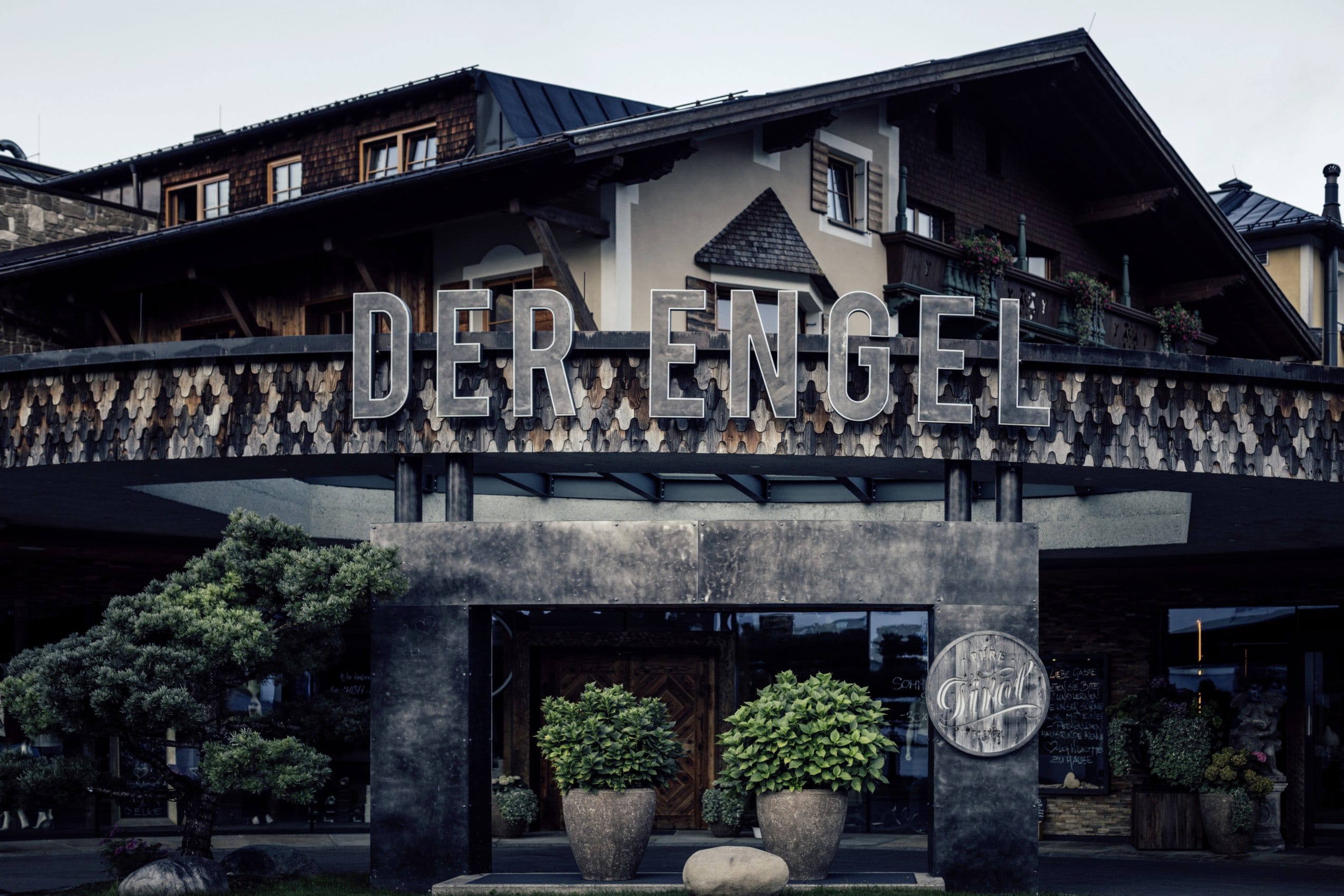 Schriftzug Der Engel über dem verschindelten Eingangsbereich des Hotels mit großen Blumentöpfen