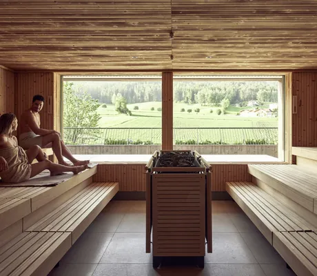 Paar sitzt in einer Sauna des Falkensteiner Hotel Kronplatz mit großem Panoramafenster