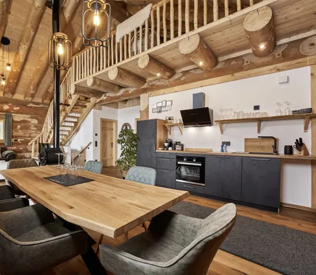 großer Esstisch und Küche in einem der modern eingerichteten Jakob Chalets mit Sofa im Hintergrund und einer Treppe zur Galerie