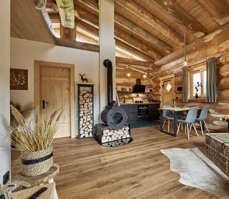 Blick in eines der modern eingerichteten Jakob Chalets mit Sofa, Esstisch, Holzofen und Küchenzeile im Hintergrund