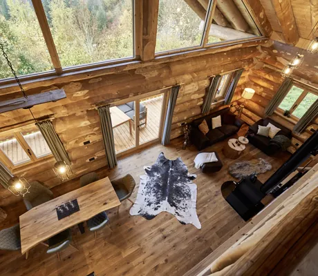 Blick von der Galerie in den Wohn- und Essbereich eines der Jakob Chalets mit großem Esstisch, Fellteppichen, Holzofen und Sofaecke