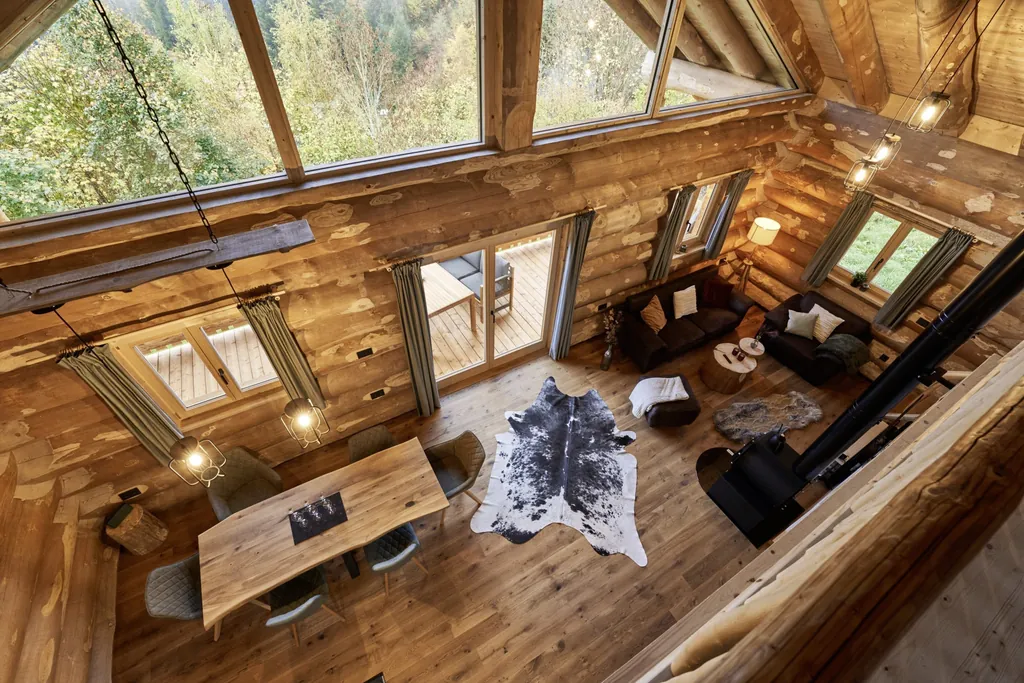 Blick von der Galerie in den Wohn- und Essbereich eines der Jakob Chalets mit gro&szlig;em Esstisch, Fellteppichen, Holzofen und Sofaecke