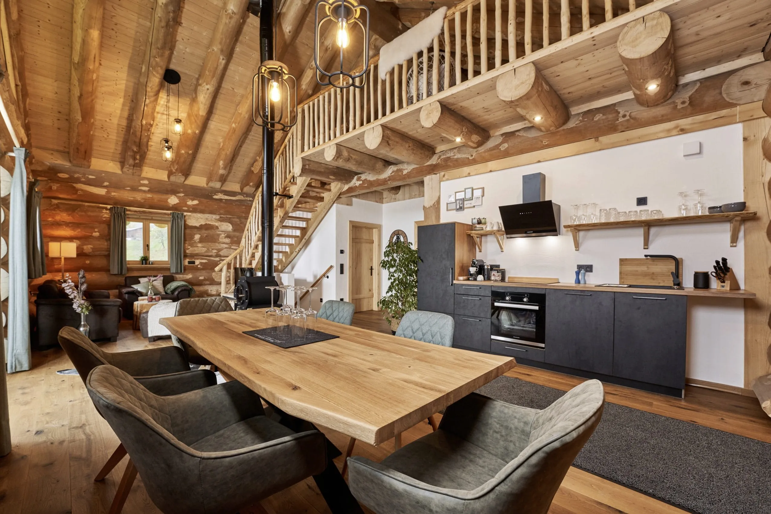 großer Esstisch und Küche in einem der modern eingerichteten Jakob Chalets mit Sofa im Hintergrund und einer Treppe zur Galerie