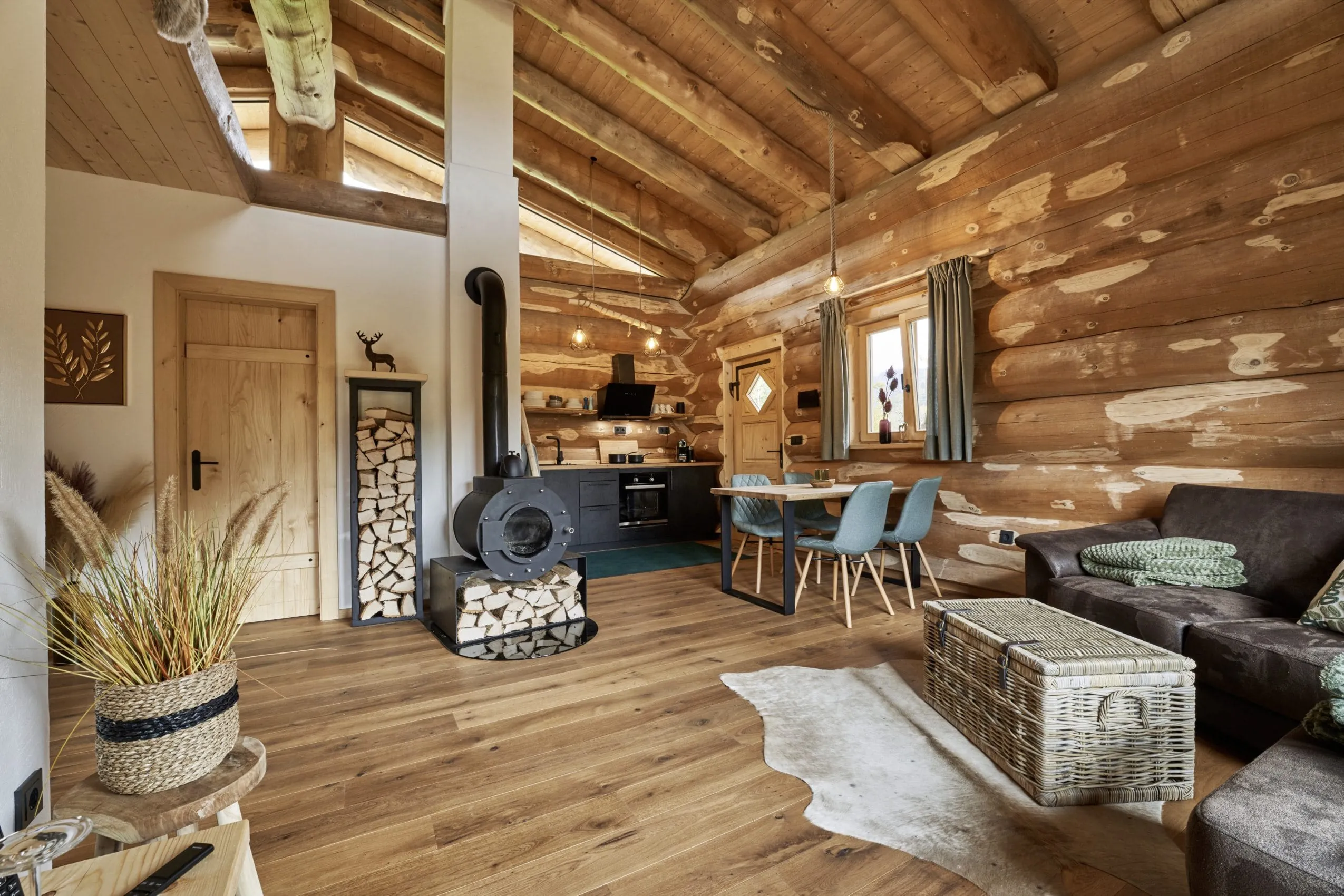 Blick in eines der modern eingerichteten Jakob Chalets mit Sofa, Esstisch, Holzofen und Küchenzeile im Hintergrund