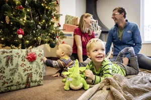 Glückliche Familie mit zwei Kleinkindern vor einem geschmückten Tannenbaum im Elldus Resort, einige Geschenke im Hintergrund