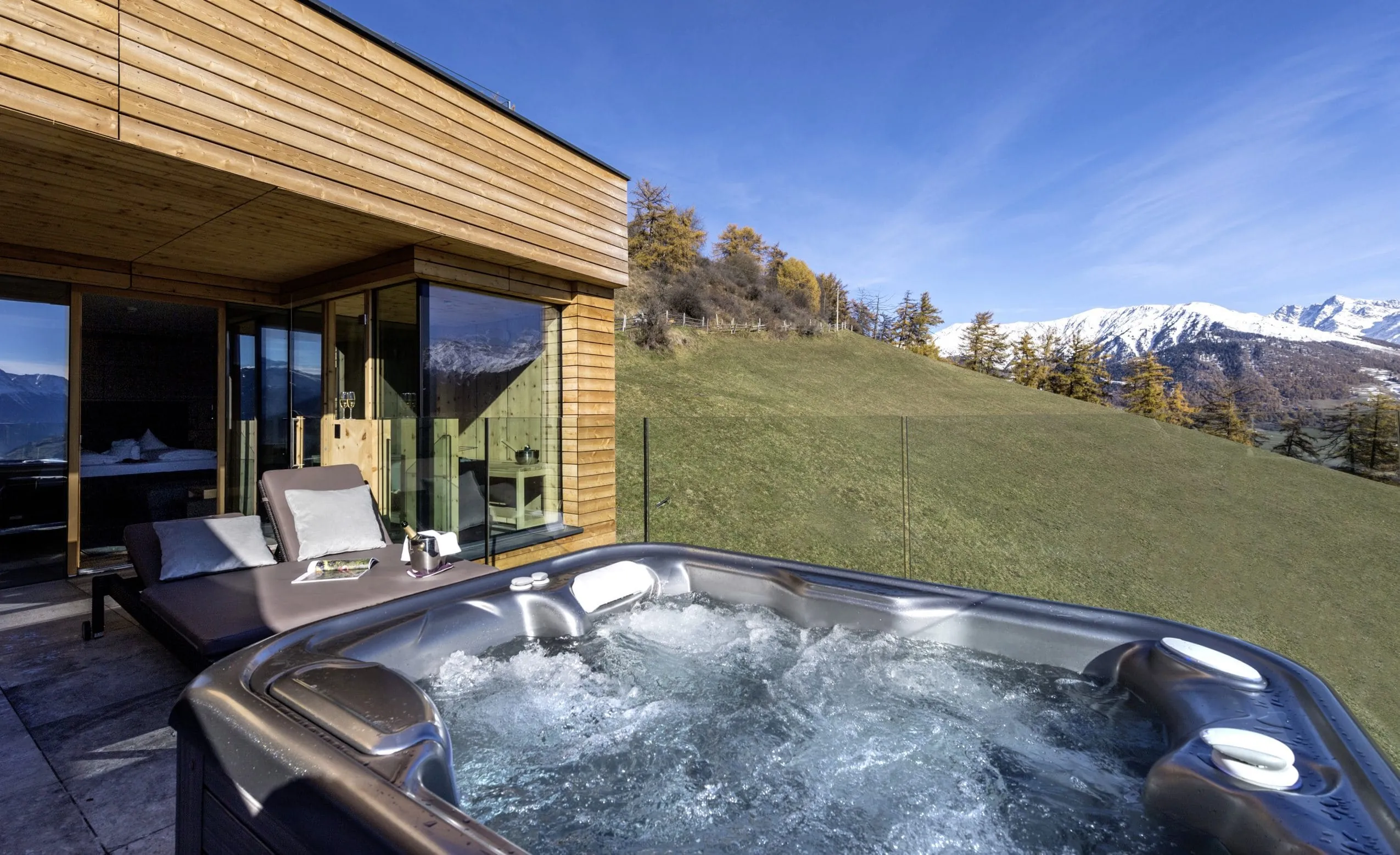 Terrasse mit eigenem Whirlpool im GERSTL Alpine Retreat mit schneebedeckten Bergen im Hintergrund.