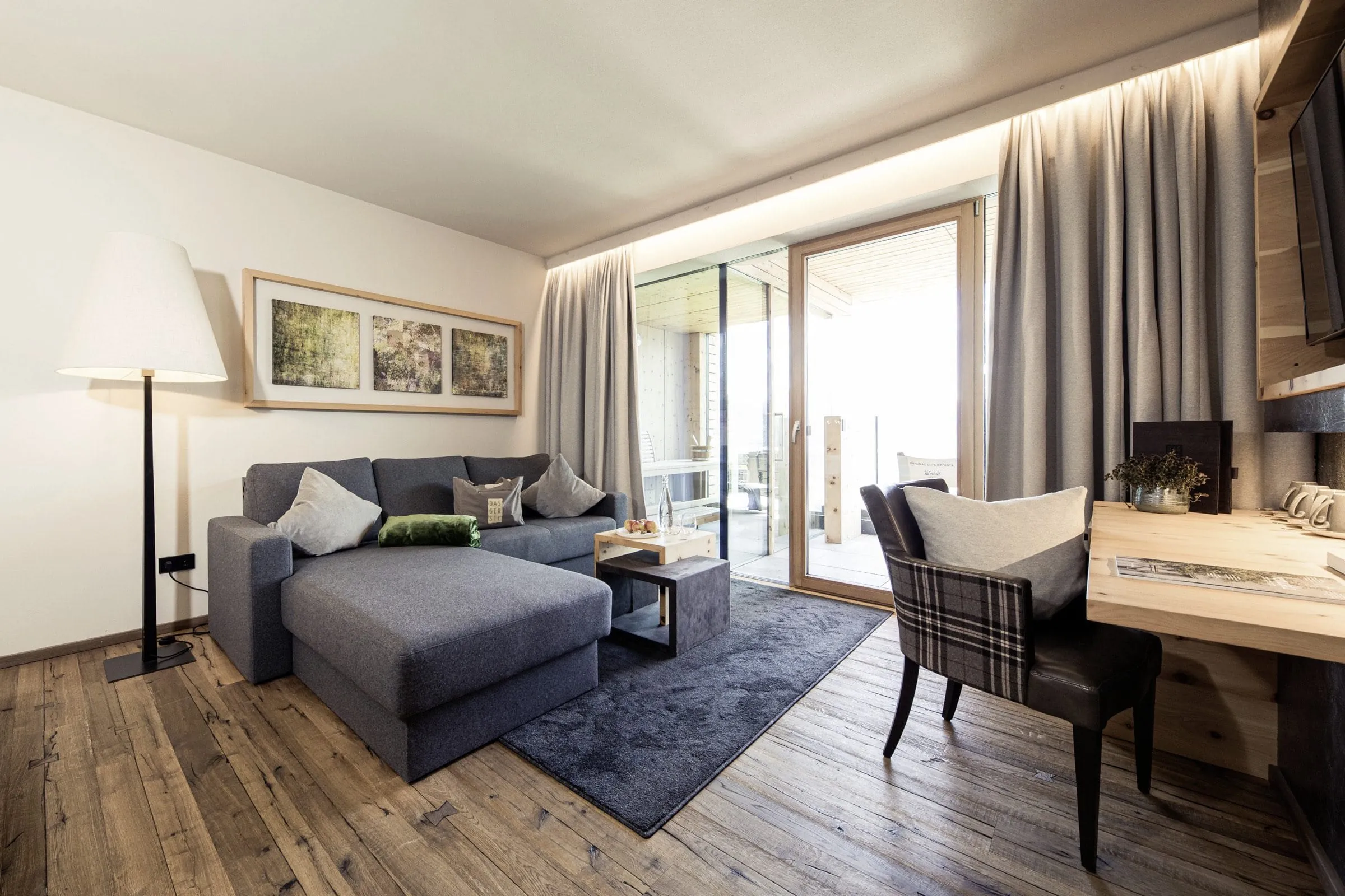 Zimmer mit Sofa und Schreibtisch im GERSTL Alpine Retreat in Mals mit grauen Vorhängen.