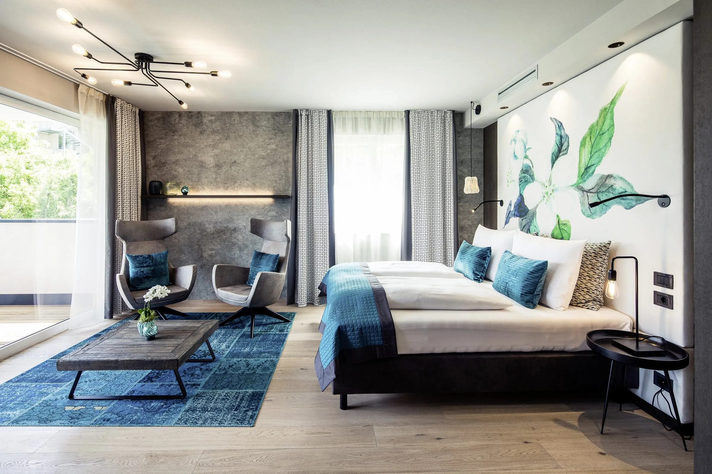 Blick in die Suite des La Maiena Meran Resort mit Samtsesseln und Doppelbett.