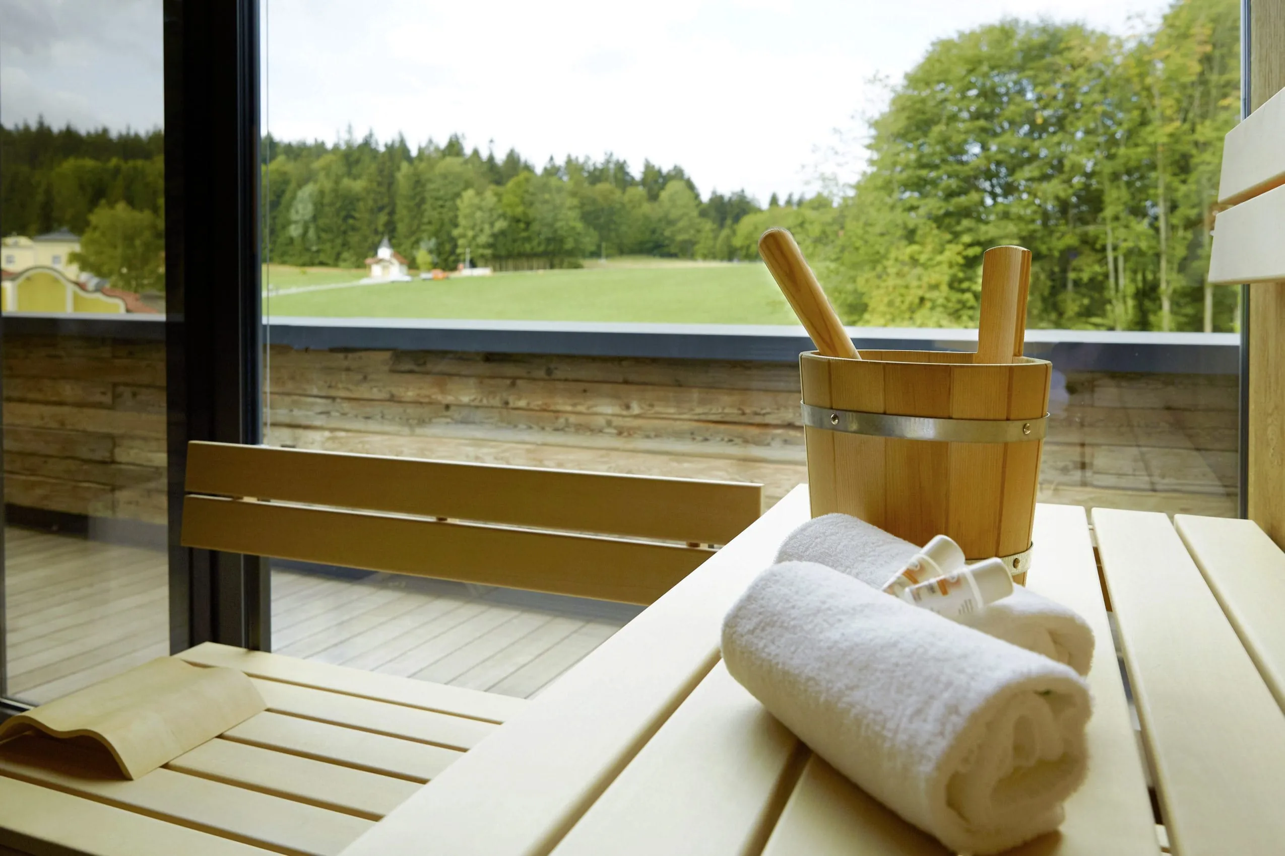 Sauna mit Handtüchern und Aufgusseimer mit Panoramablick auf grüne Wiesen und Bäume im Wellness & Naturresort Reischlhof **** Superior.