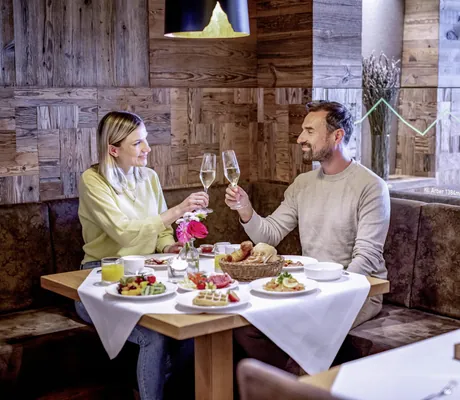 Ein Pärchen stößt im Hotel Brunner Hof in Arnschwang mit einem Gläschen Sekt an einem gedeckten Frühstückstisch an.