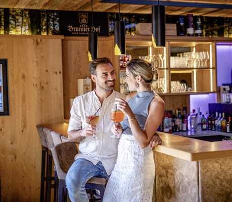 Ein Pärchen genießt einen Longdrink an der Hotelbar des Brunner Hof in Arnschwang, der mit warmen Licht und Holz ausgestattet ist.