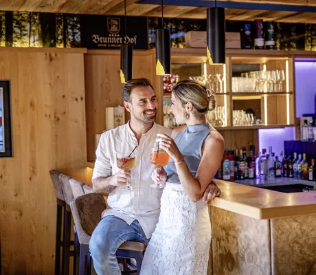 Ein Pärchen genießt einen Longdrink an der Hotelbar des Brunner Hof in Arnschwang, der mit warmen Licht und Holz ausgestattet ist.