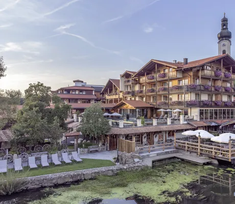 Außenfassade des Natur- und Wellnesshotel Brunner Hof in Arnschwang mit Geranien an den Balkonen und Kirchturm im Hintergrund.
