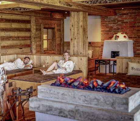 Ein Pärchen entspannt auf den Holz-Liegen im Wellnessbereich vor dem Effektkamin.