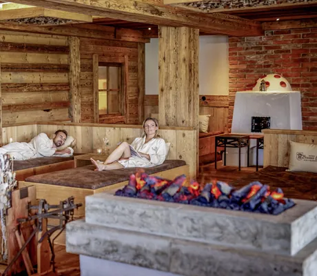 Ein Pärchen entspannt auf den Holz-Liegen im Wellnessbereich vor dem Effektkamin.