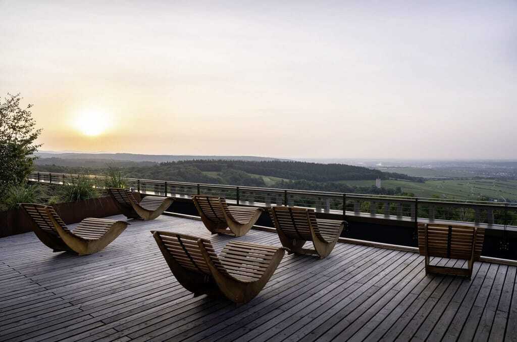 Eine Sitzgruppe mit Liegestühlen aus Holz auf der Rooftop-Terrasse des WALD.WEIT Rheingau Hotel & Retreat bei Sonnenuntergang.