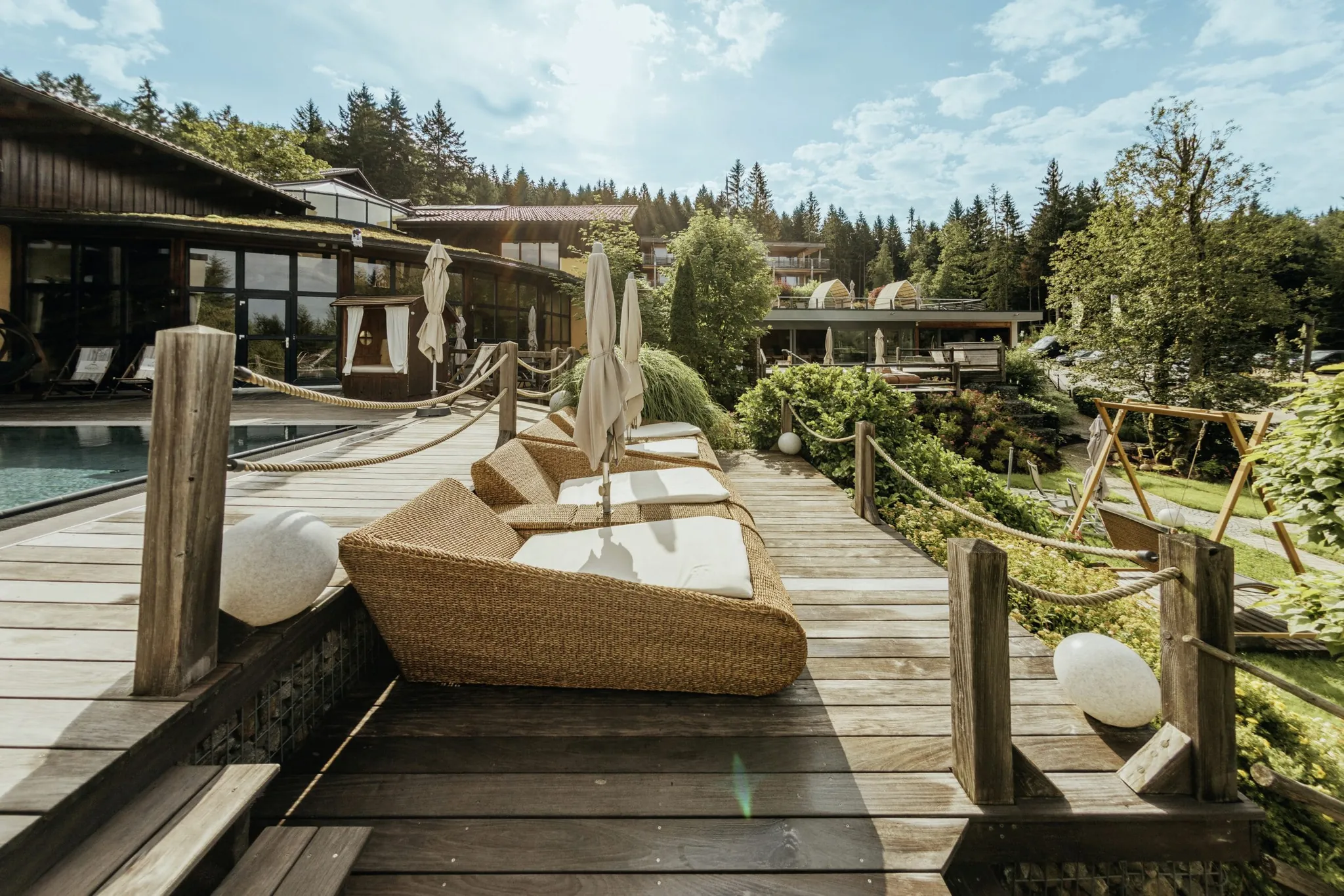 Outdoor-Wellnessbereich des Wellnesshotel Riedlberg mit Pool, gemütlichen Liegen auf einer Holzterrasse und Blick ins Grüne