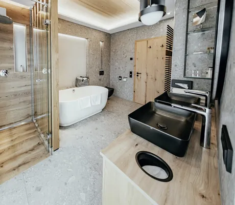 Modernes Badezimmer im Wellnesshotel Riedlberg mit freistehender Badewanne, Regendusche und schwarzen Waschbecken