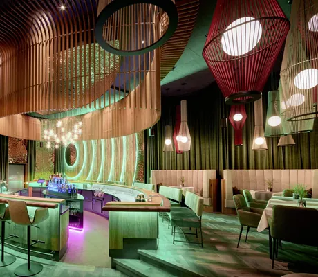 Stilvolle Bar im Wellnesshotel Riedlberg mit geschwungenem, ovalem Holzdesign über der Theke, leuchtenden Hängelampen und gemütlichen Sitzgruppen