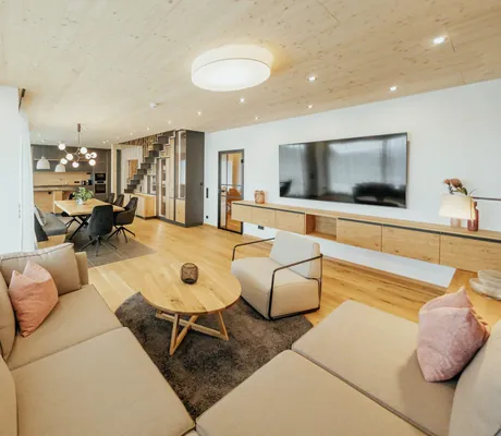 Geräumiger, moderner Wohnbereich mit Holzdetails, großem Sofa und Essbereich mit Küche in einem Chalet des Wellnesshotel Riedlberg