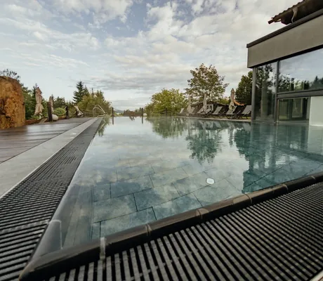 Outdoorpool des Wellnesshotel Riedlberg mit Sonnenliegen und -schirmen, umgeben von Natur