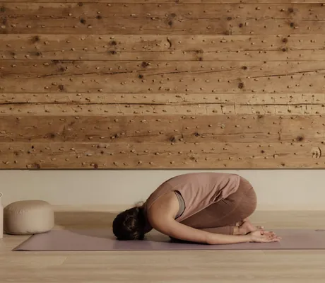 Frau hockt in Yogapose auf der Yogamatte vor Holzwand in der Schlossanger Alp