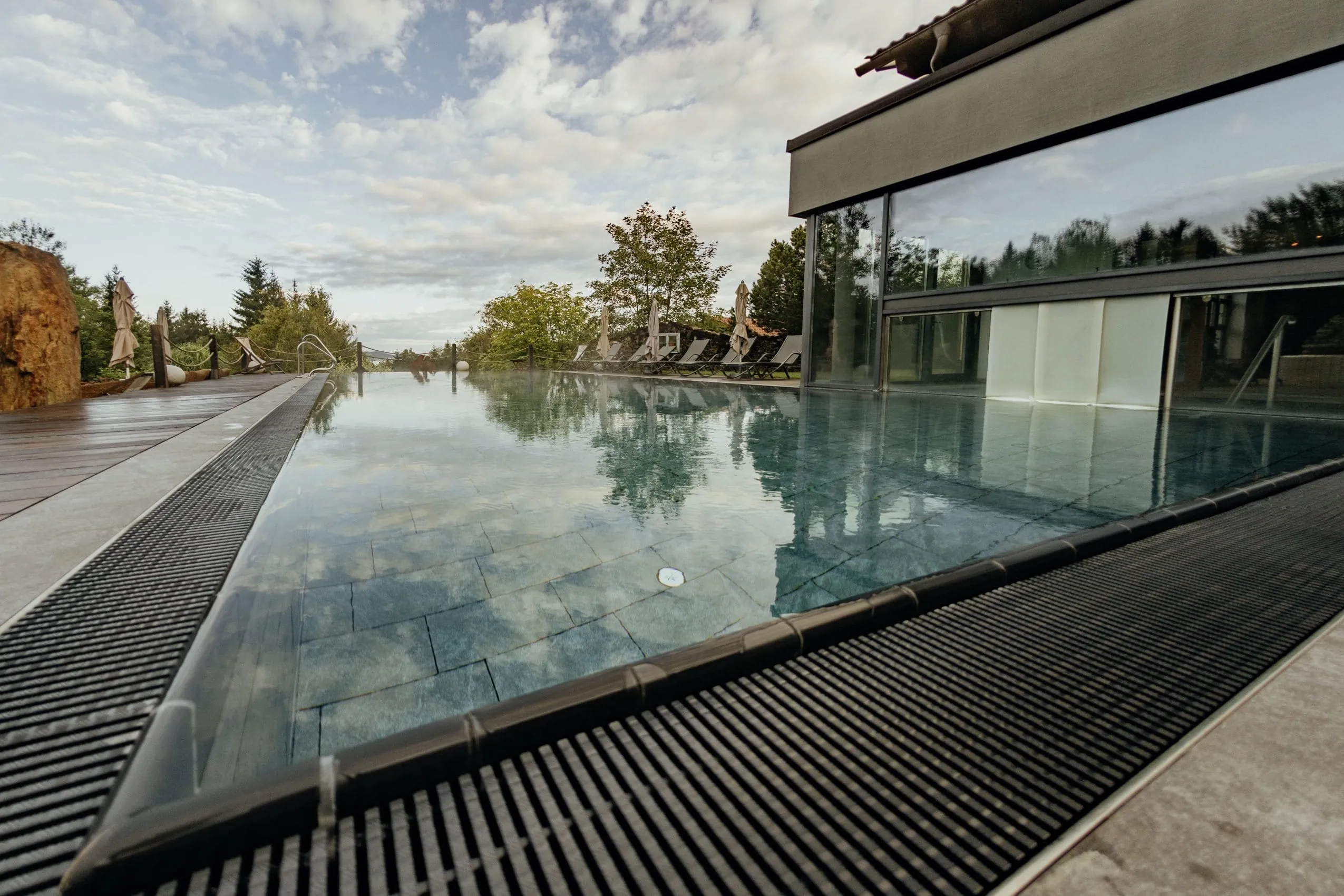 Outdoorpool des Wellnesshotel Riedlberg mit Sonnenliegen und -schirmen, umgeben von Natur