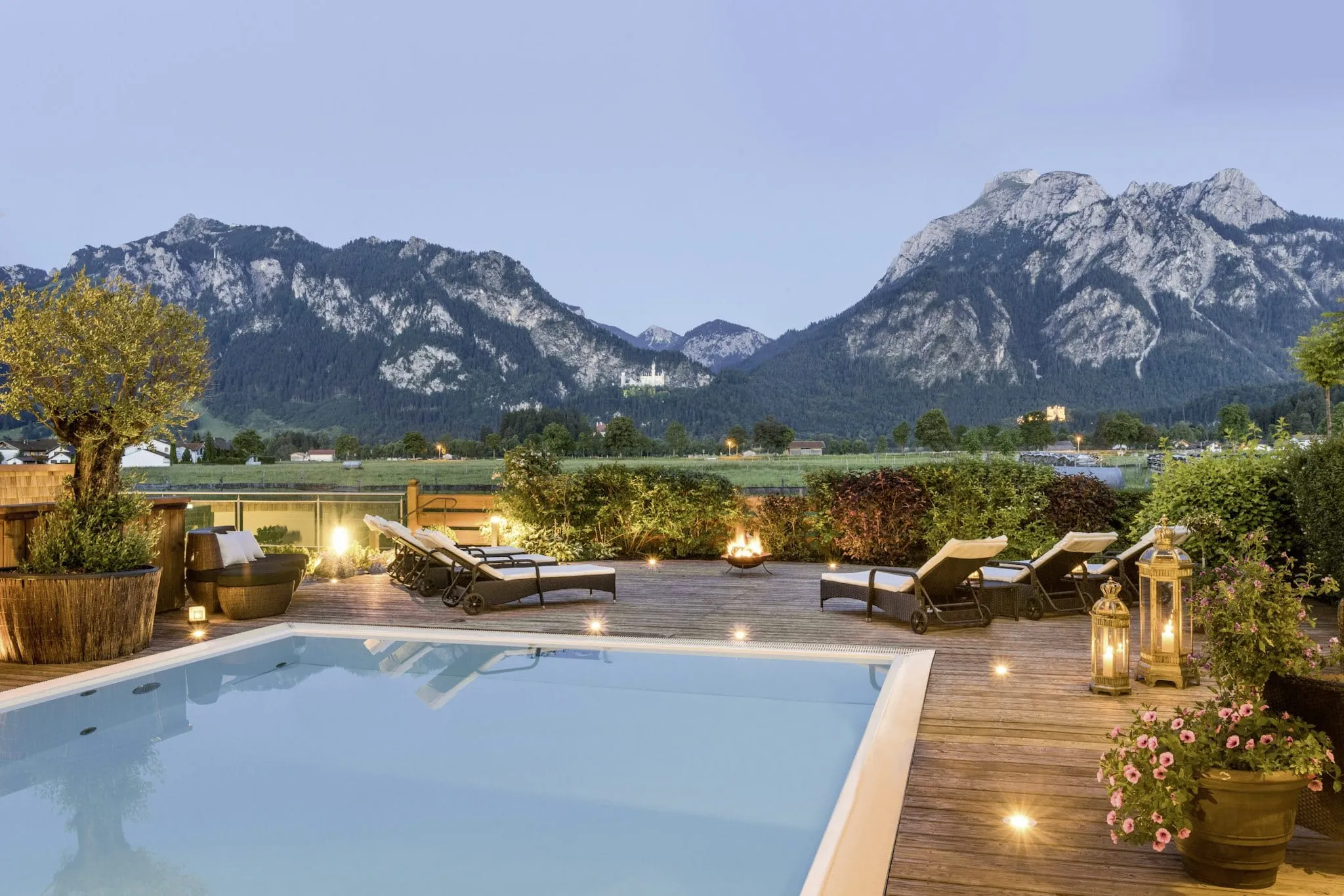 Blick vom beleuchteten Outdoorpool des Yoga-Hotels Das Rübezahl auf Schloss Neuschwanstein in der Abenddämmerung