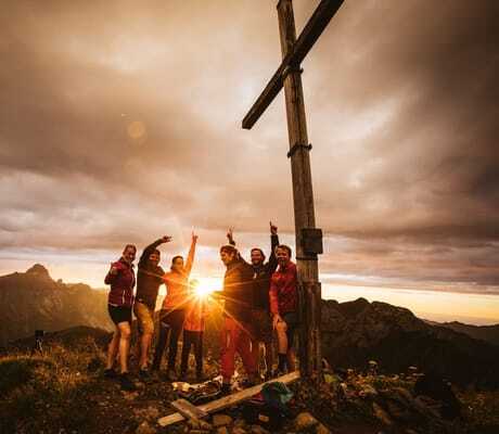 Glückliche Wandergruppe neben einem Gipfelkreuz in der Nähe des Berghaus Schröcken