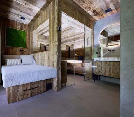 Modern eingerichteter Bereich der Ziegelberg Chalets mit Holzwänden, einer gemütlichen Sitzbank, Sauna und rundem Spiegel über Stein-Waschbecken