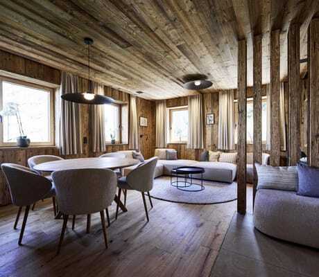 Gemütlicher Wohn- und Essbereich in den Ziegelberg Chalets mit Holzwänden und -decke, rundem Esstisch, gepolsterten Stühlen und Lounge-Ecke mit Sofa