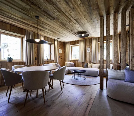 Gemütlicher Wohn- und Essbereich in den Ziegelberg Chalets mit Holzwänden und -decke, rundem Esstisch, gepolsterten Stühlen und Lounge-Ecke mit Sofa