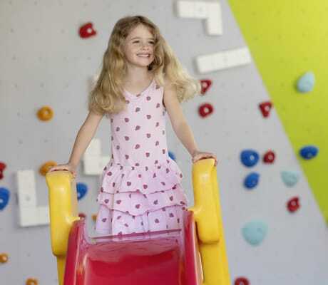 Mädchen auf rot-gelber Rutsche im Spielzimmer im Familotel Ottonenhof mit Boulderwand im Hintergrund