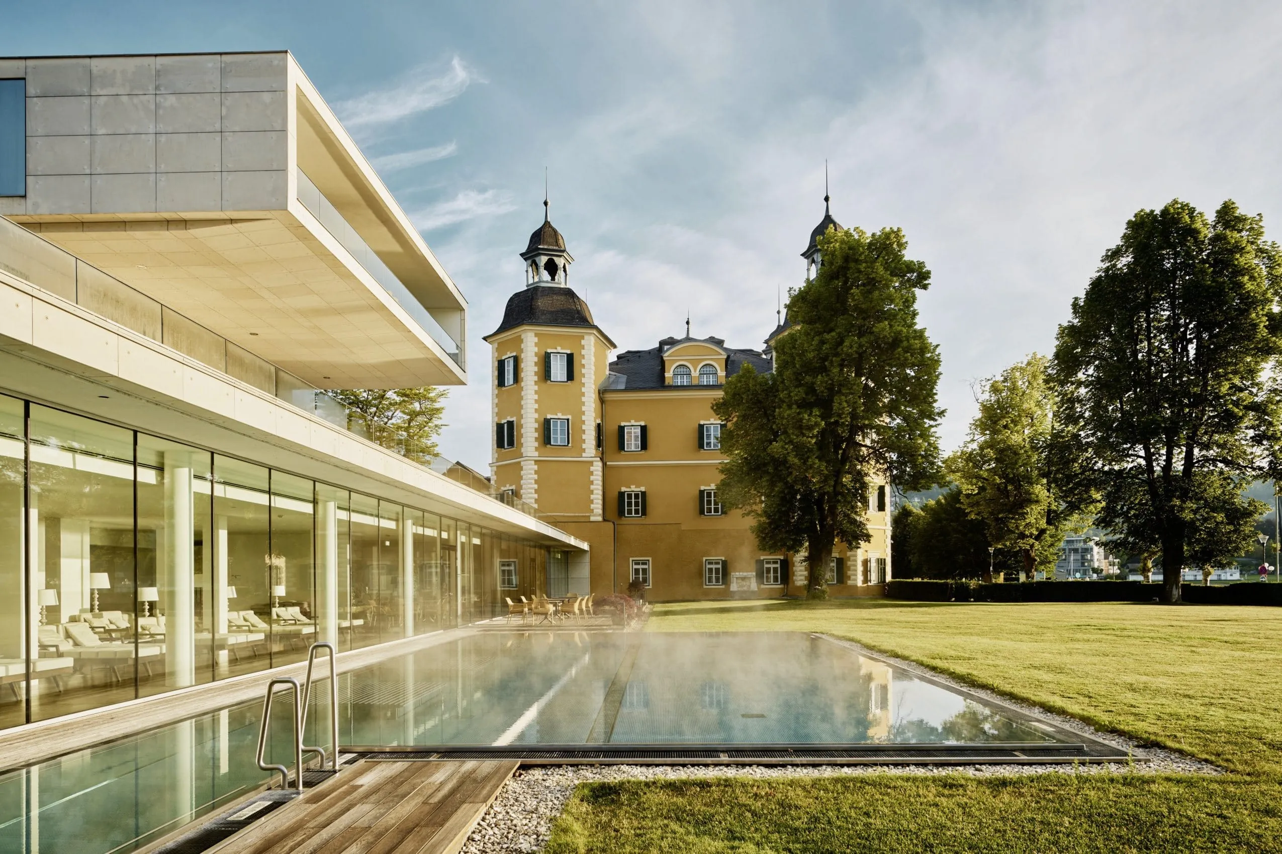 Das Falkensteiner Schlosshotel Velden mit beheiztem Pool und der markant gelben Schlossfassade.