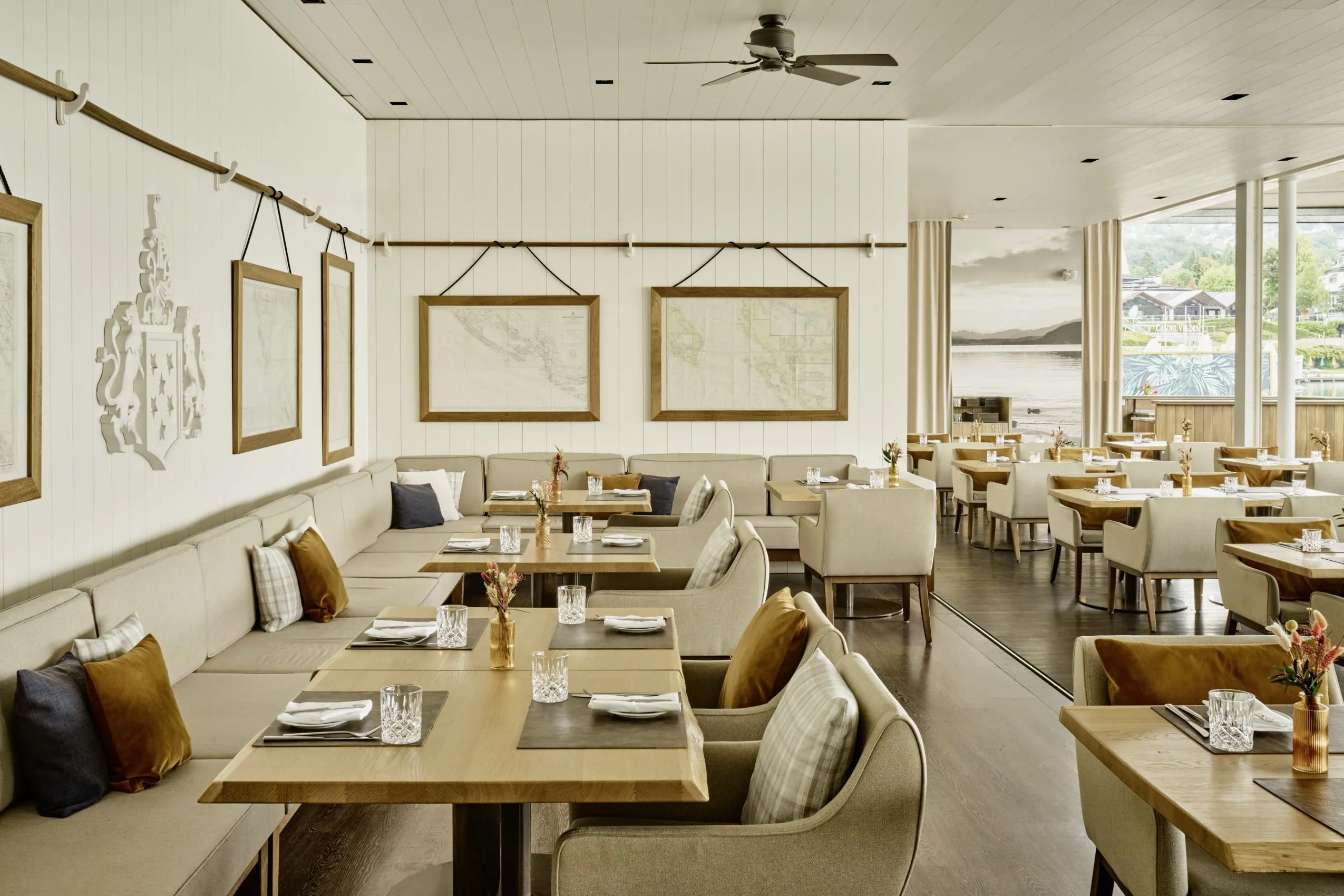 Restaurant im Falkensteiner Schlosshotel Velden mit zeitlos weiß-beigen Möbeln, Sitzbänken und Wänden.
