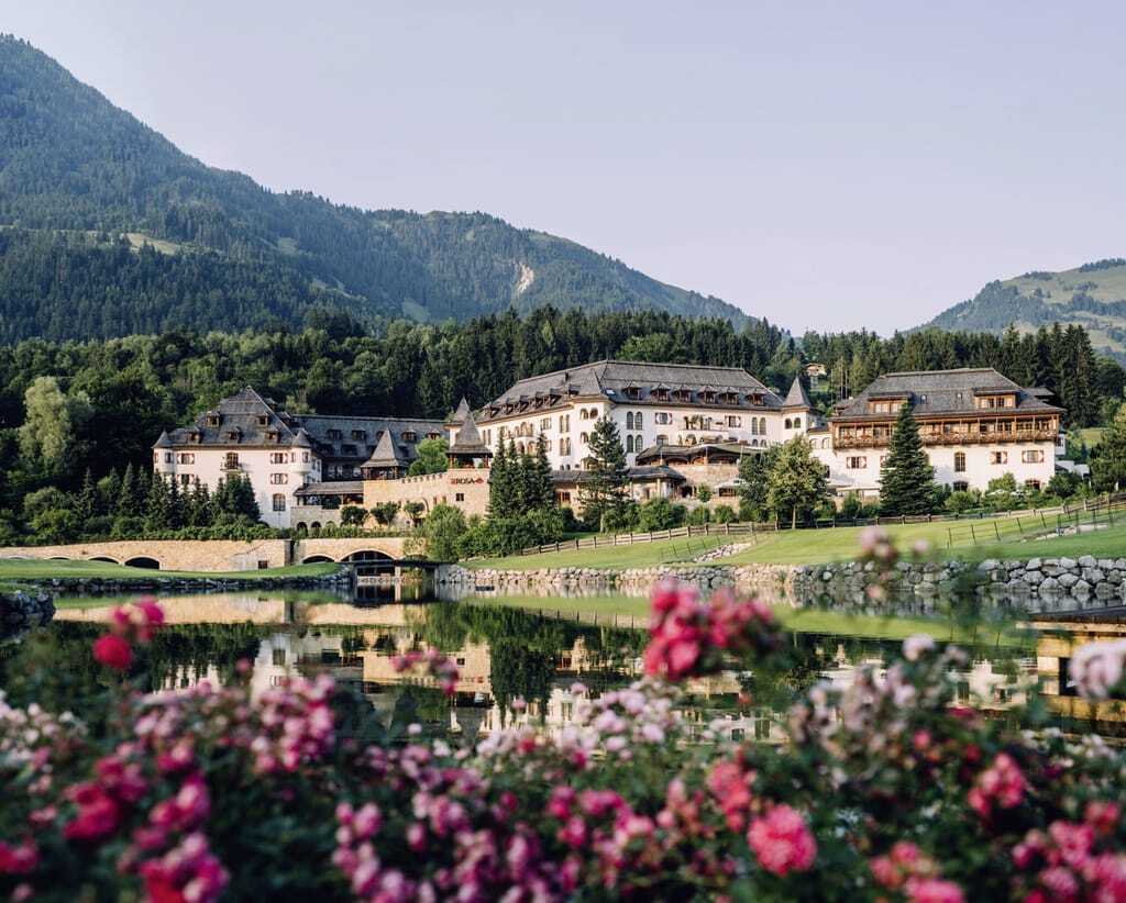 Die Gesamtansicht des Schlosshotels Kitzbühel in Tirol mit Türmchen und weiß roten Fenstern.