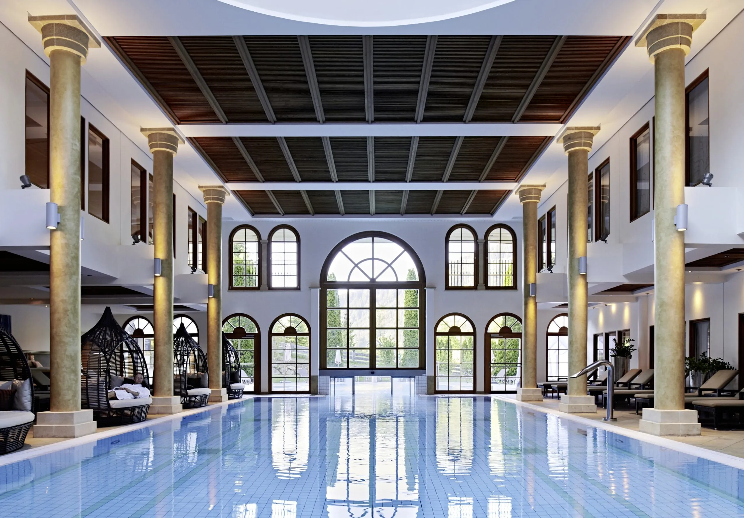 Der Innenpool im Schlosshotel Kitzb&uuml;hel mit imposanten S&auml;ulen und Rundbogenfenstern.