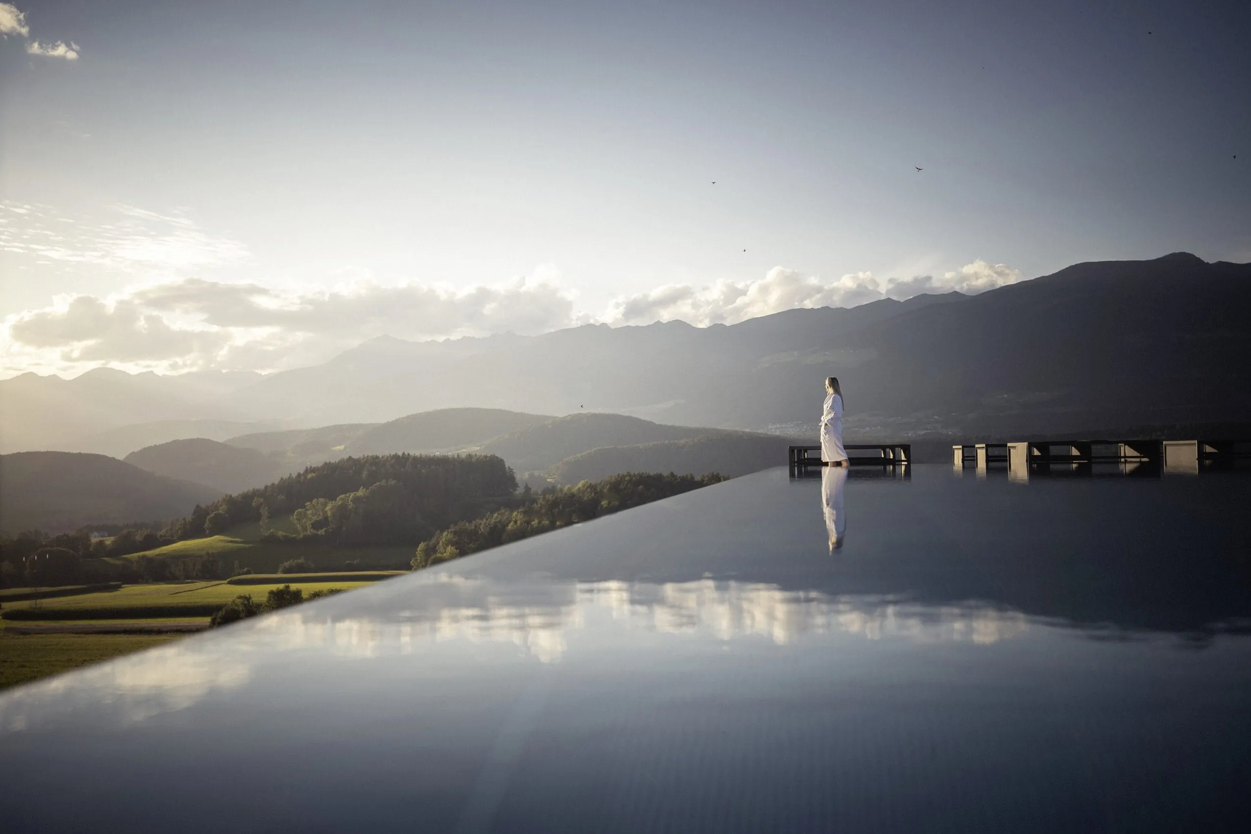 Eine Frau im Bademantel steht am Rande des Infinitypools im Hotel Winkler und blickt über die Ferne.