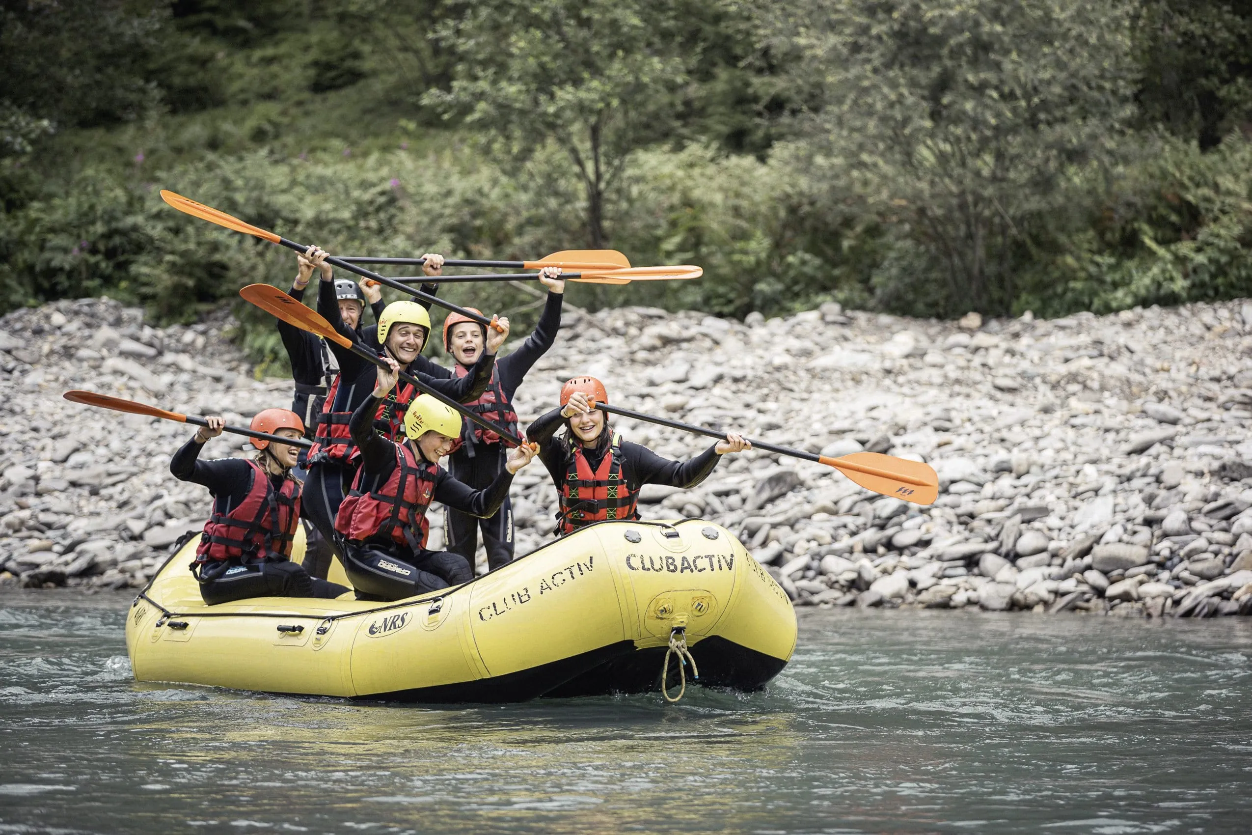 Eine Gruppe Jugendlicher sitzen in einem gelben Rafting-Boot und paddeln um die Wette.