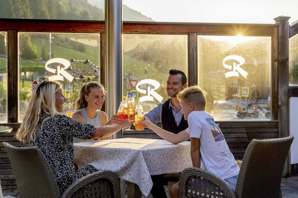 Eine Familie stößt mit Drinks im Restaurant an im Good Life Resort Riederalm in Leogang.
