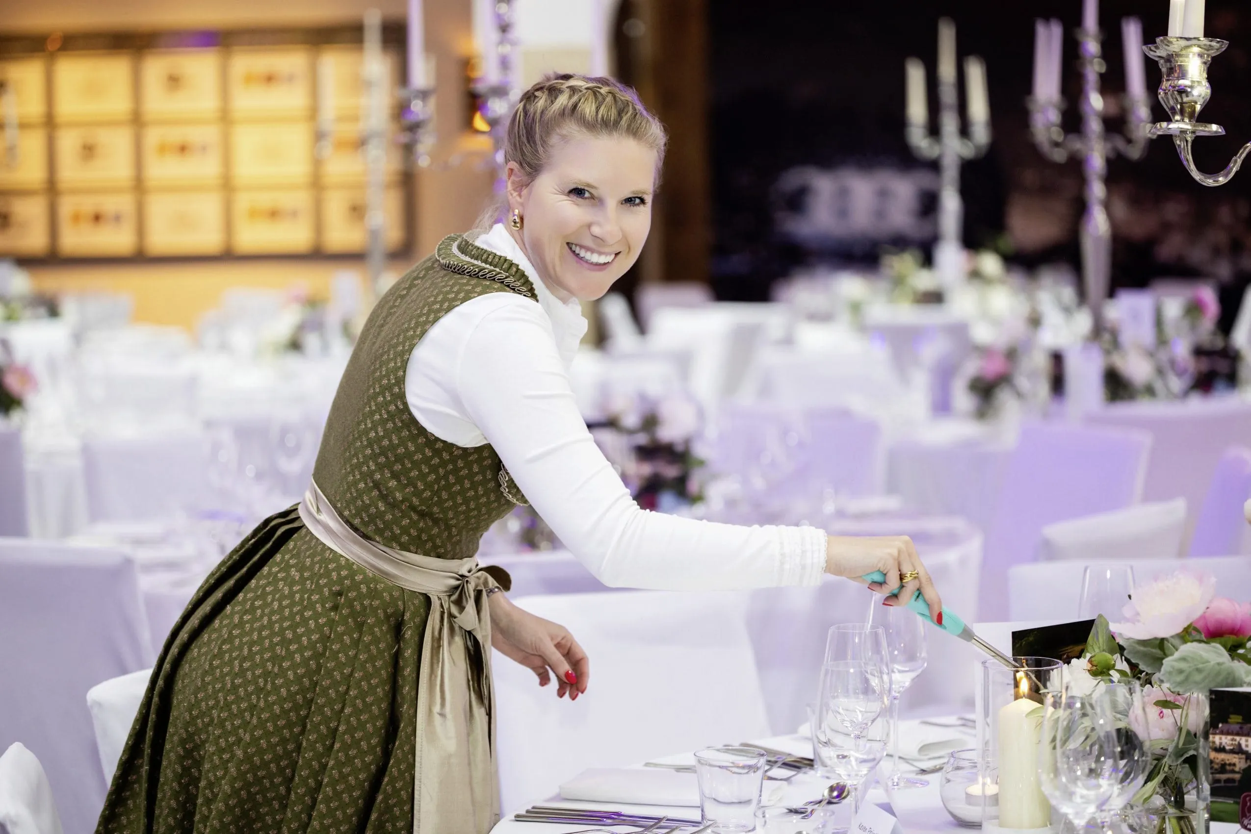Junge Frau in schickem Dirndl z&uuml;ndet eine Kerze auf der Tischdekoration der Wellness Aphrodite an