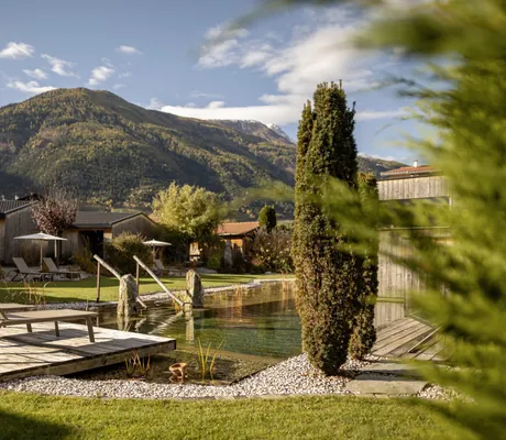 Sonnenliegen auf einem Holzdeck am Badeteich des Amolaris und Blick auf die Berge