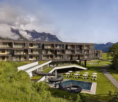 Außenansicht des Falkensteiner Family Hotel Montafon mit moderner Holzfassade, Pool, Wasserrutsche und Bergkulisse im Hintergrund