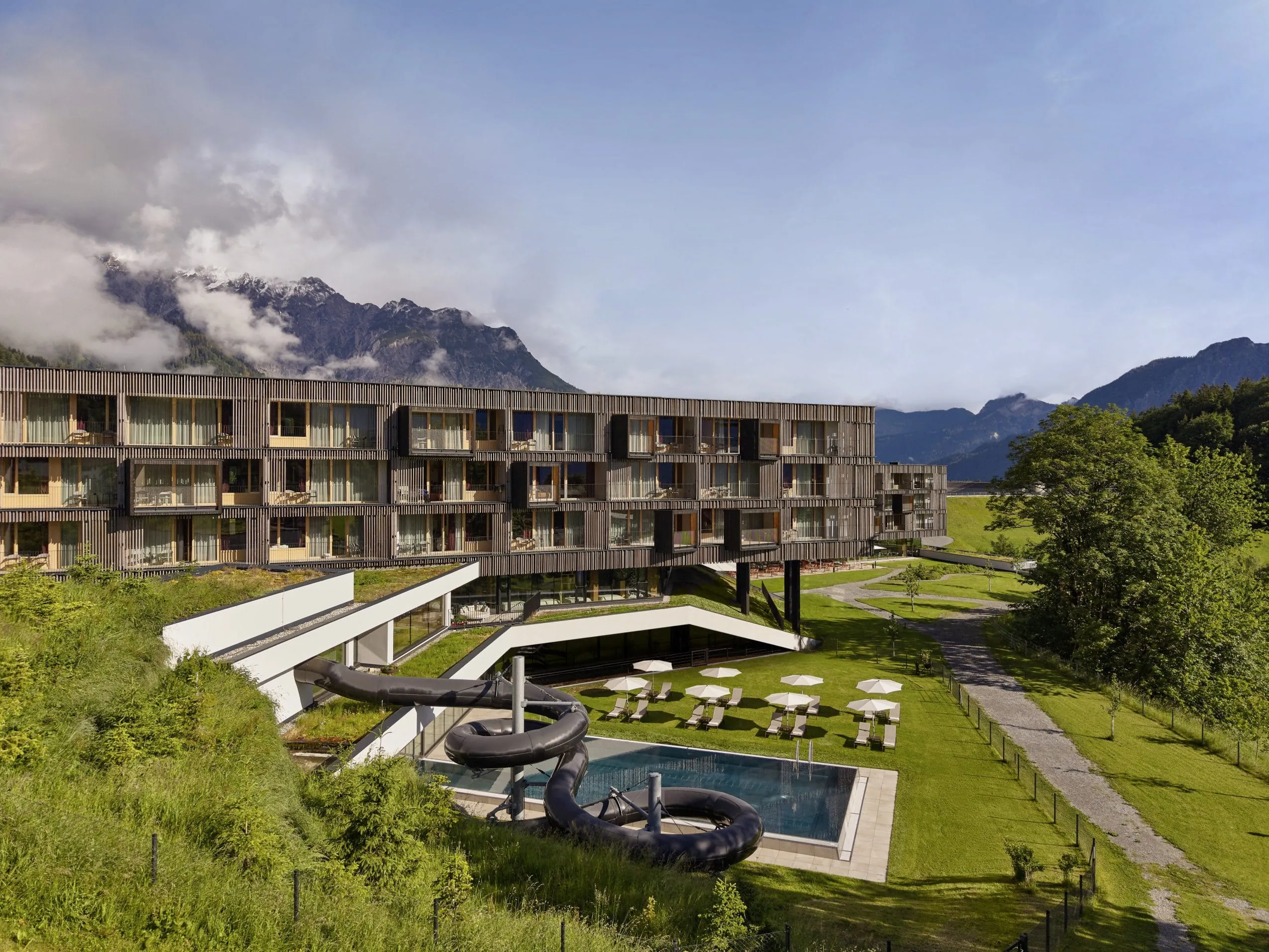 Außenansicht des Falkensteiner Family Hotel Montafon mit moderner Holzfassade, Pool, Wasserrutsche und Bergkulisse im Hintergrund
