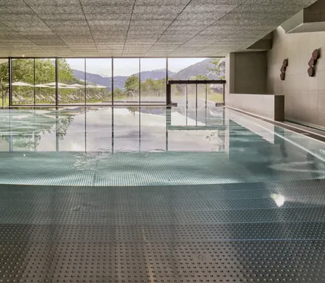 Indoorpool mit großen Panoramafenstern und Blick auf Liegewiese und Berge im Falkensteiner Family Hotel Montafon