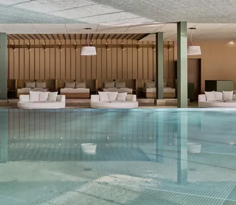 Indoorpool mit mehreren Liegeflächen, runden Sofas und Holzwänden im Falkensteiner Family Hotel Montafon