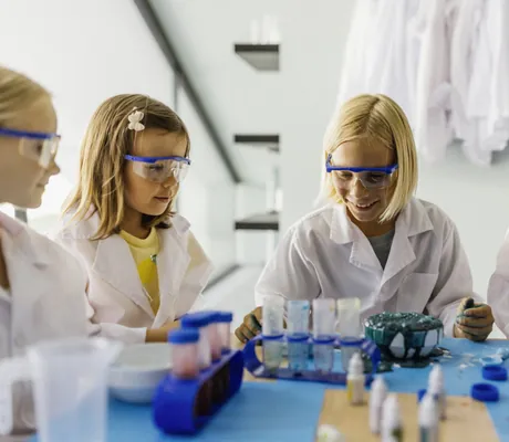 Kinder im Labor experimentieren mit Schutzbrillen und Laborkitteln an einem Tisch mit bunten Flüssigkeiten im Falkensteiner Family Hotel Montafon