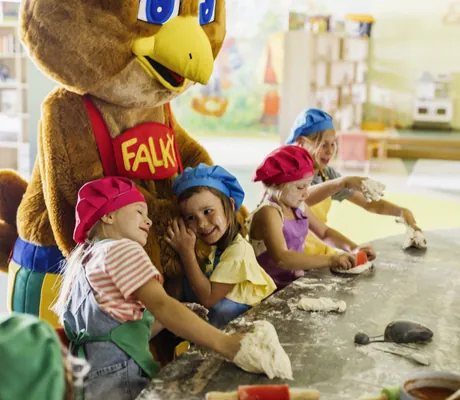 Kinder backen mit dem Maskottchen Falky und haben sichtlich Spaß beim Kneten von Teig im Falkensteiner Family Hotel Montafon