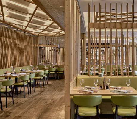 Modernes Restaurant mit Holzelementen, grünen Polsterstühlen und gedeckten Tischen im Falkensteiner Family Hotel Montafon