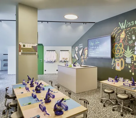 Kinderfreundliches Labor mit Mikroskopen, buntem Wanddesign und Tischen für Experimente im Falkensteiner Family Hotel Montafon